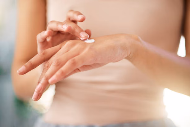 Close-up of a woman applying white moisturising cream to the back of her hand in soft natural light